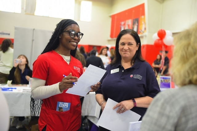 St. John's nursing student in red scrubs with woman in navy shirt