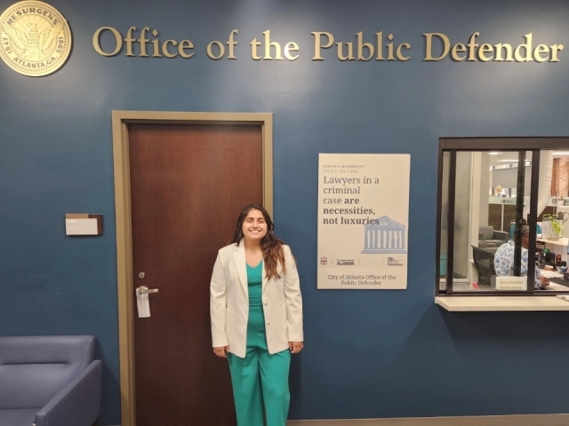 Nicole Castillo Guiracocha stands in her office's waiting room under a sign reading Office of the Public Defender.