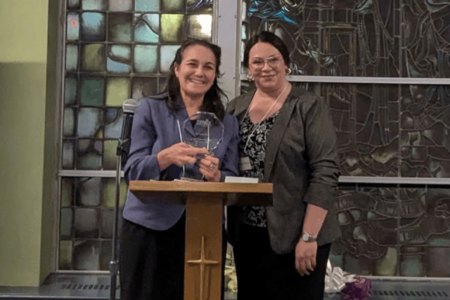 Women holding an award next to another woman at the podium