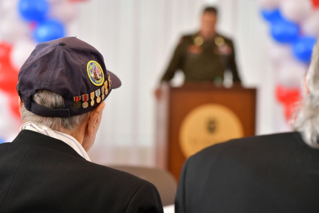 veteran male with hat looking at speaker at podium 