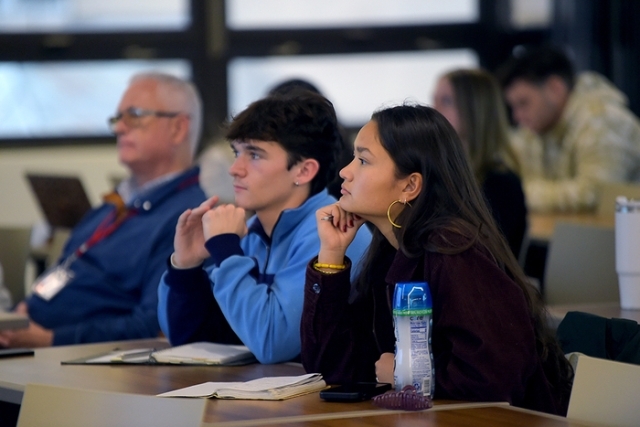 Three students listening at their desks in a lecture hall