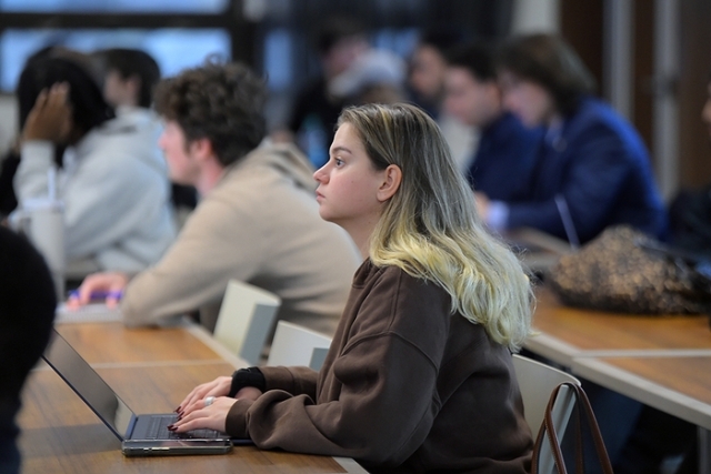 Female student listening in lecture hall while typing on her computer