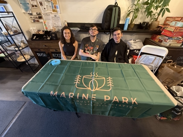Three individuals sitting at a table with a green table cloth 