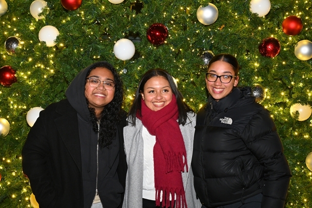 Three students smiling in front of giant Christmas tree