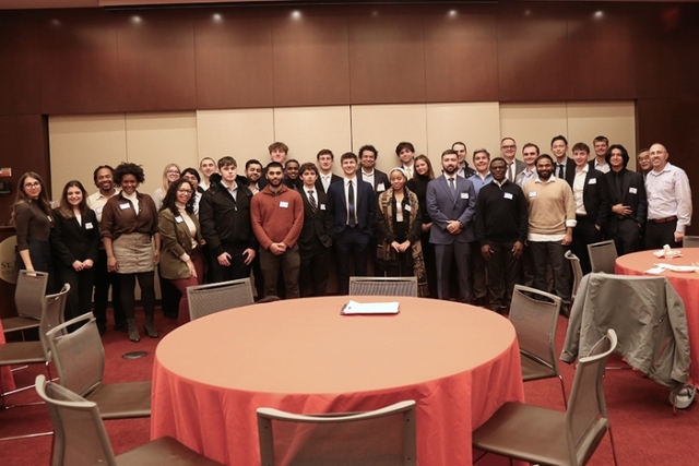 Large group of students and faculty gathered for a formal academic or networking event in a conference space.