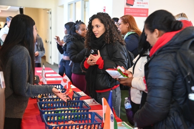 Students gather around a table with international snacks while speaking with a representative during a campus cultural event.