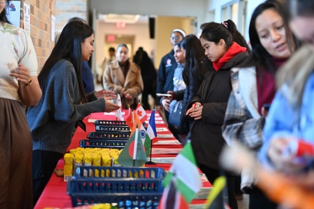 Students browse international snacks displayed on a long table decorated with small country flags during a campus event.