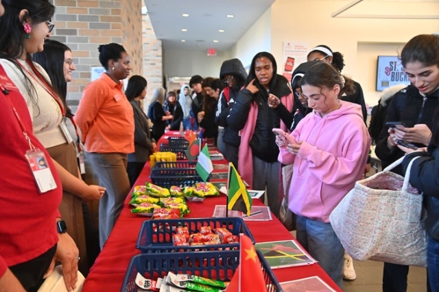 Students browse international snacks displayed on a long table decorated with small country flags during a campus event.