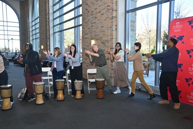 Two musicians perform on traditional drums in front of a fireplace at a campus cultural program.