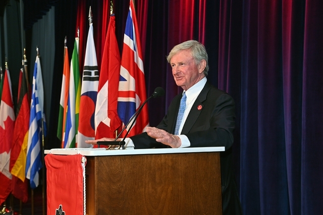 Speaker standing at a podium with international flags behind him, addressing the audience during the Insurance Leader of the Year Award Dinner.