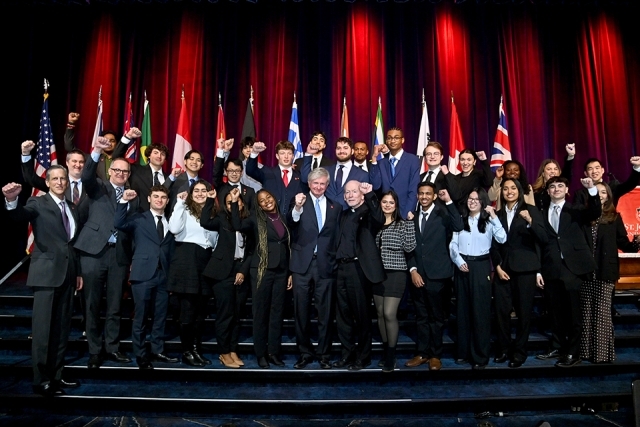 Large group of students and university leaders posing together on stage with raised fists in a celebratory group photo.