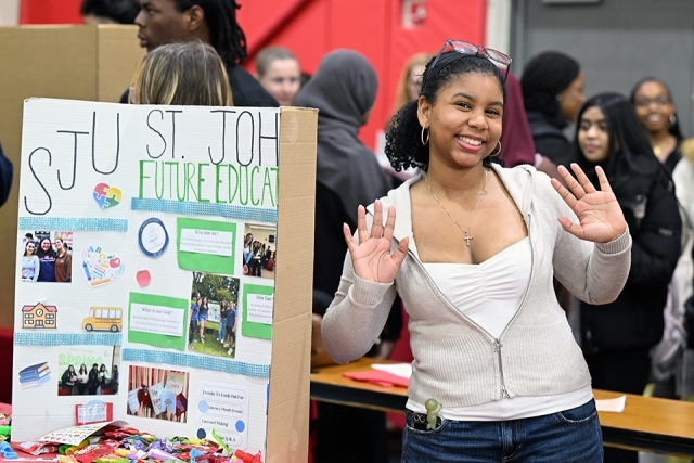 Student waving next to a presentation board