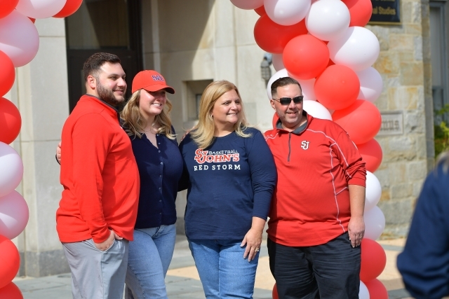 Candid shot of four people under a balloon arch in front of St. Augustine Hall.
