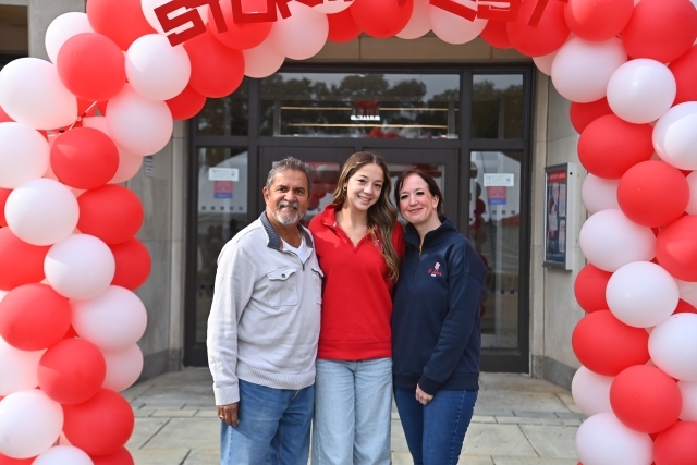 Three people under a red and white balloon arch.