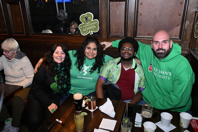 Group of St. John’s University alumni wearing green and posing together at a St. Patrick’s Day celebration indoors