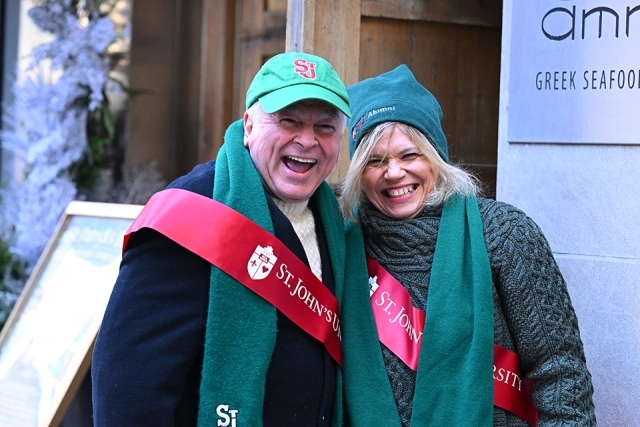 Two St. John’s University alumni wearing red sashes and hats smiling during a St. Patrick’s Day parade