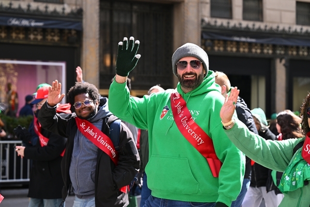 St. John’s University alumni waving and smiling while walking in a St. Patrick’s Day parade