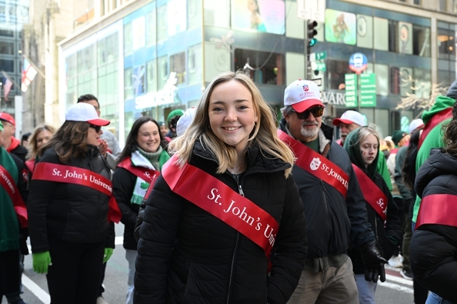 St. John’s University student wearing a red sash smiling while walking in a New York City St. Patrick’s Day parade