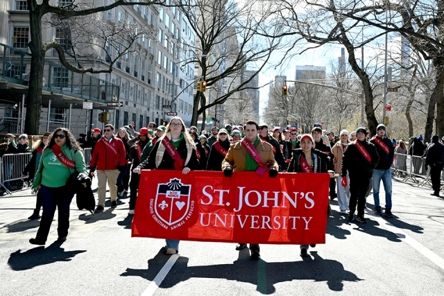 St. John’s University students and alumni holding a red banner while marching down a city street during a parade