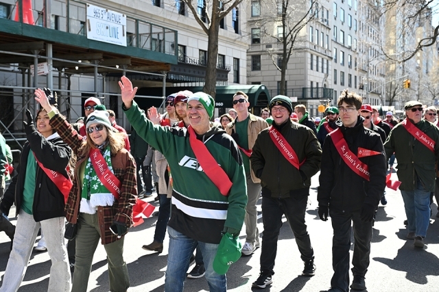 St. John’s University alumni waving and smiling while walking together in a city parade