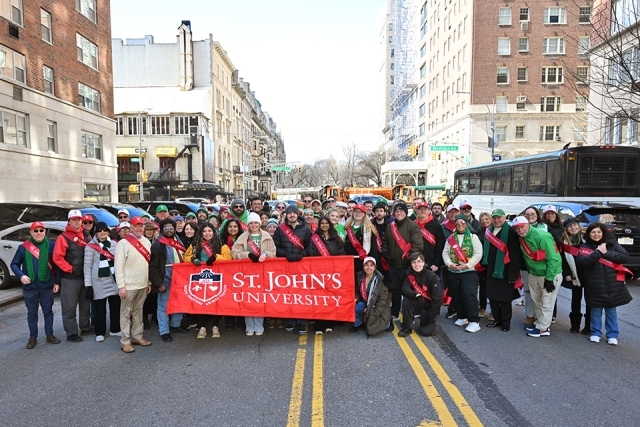 Large group of St. John’s University students and alumni posing together with a banner on a New York City street