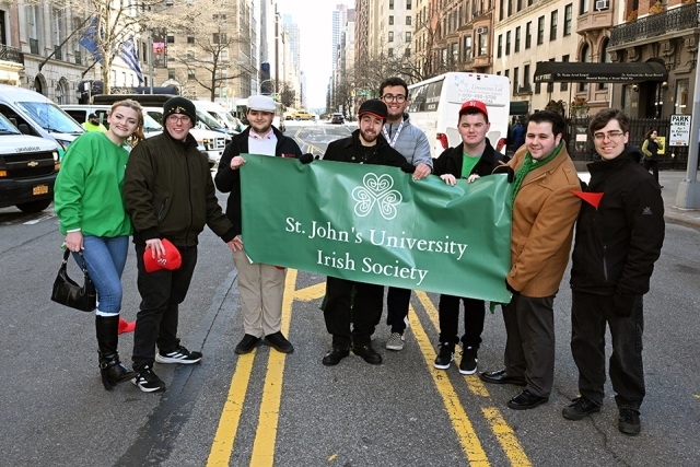Large group of St. John’s University students and alumni posing together with a banner on a New York City street
