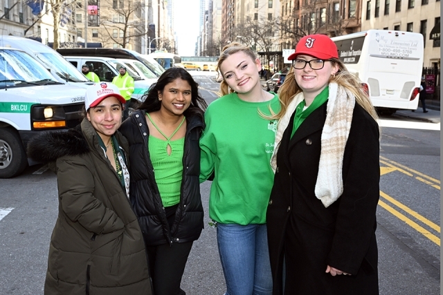 group of St. John’s University students and alumni posing together with a banner on a New York City street