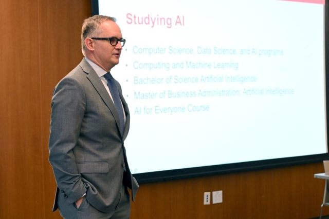 Man speaking in front of a projector screen 