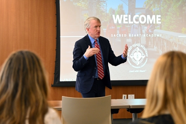 Man speaking in front of a projector screen 