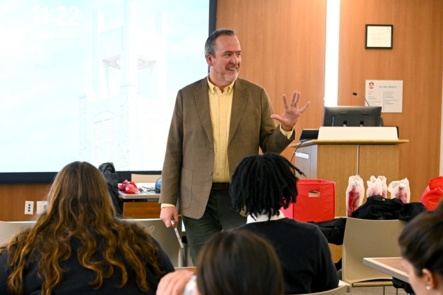 Man speaking in front of a projector screen 