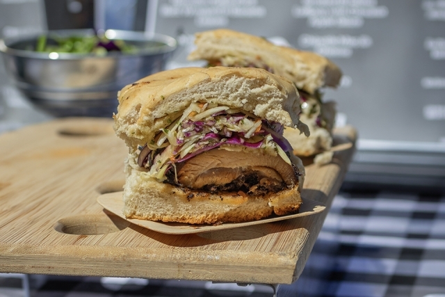 Close-up of a grilled chicken sandwich topped with coleslaw on a wooden serving board.