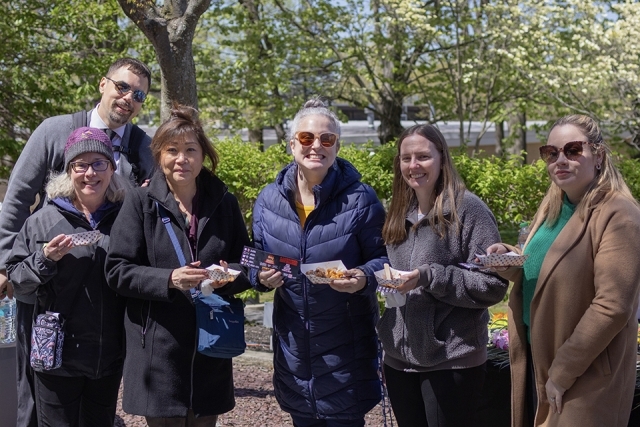 Group of adults standing together outdoors, each holding small food samples at a campus event.