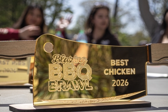 Close-up of a gold cleaver-shaped trophy engraved “Blazing BBQ Brawl Best Chicken 2026” on display at an outdoor event.