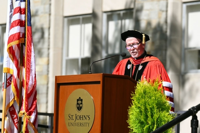 Graduate wearing a decorated stole smiles while receiving a diploma during St. John’s University commencement.
