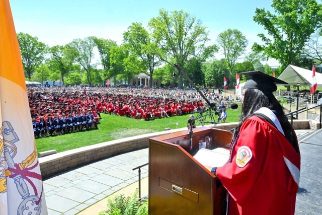 St. John’s University graduate wearing honor cords poses on stage during commencement ceremony.