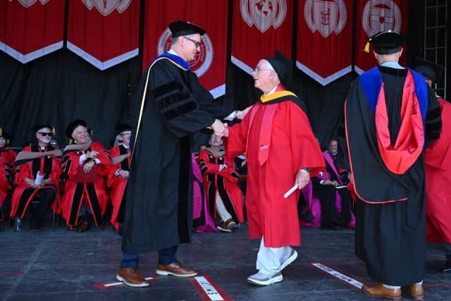 Graduate shakes hands with university official while crossing the stage at St. John’s University commencement ceremony.