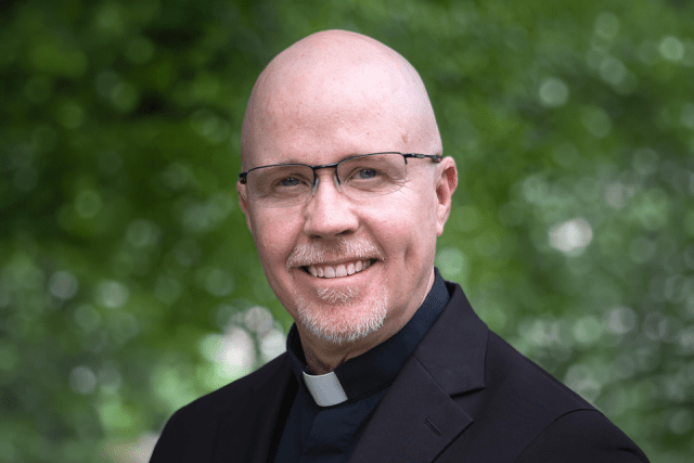 Portrait of Father Fitzgerald wearing a clerical collar outdoors.