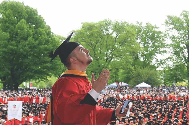 Male student walking across stage while looking up