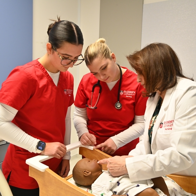 Nursing students in red scrubs working with faculty in white scrub