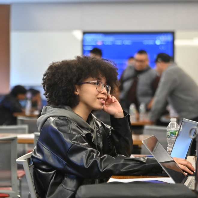 Young woman in a leather jacket sitting in a classroom setting with a labtop