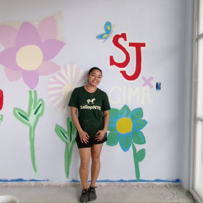 Student in front of a painted wall with SJ initials