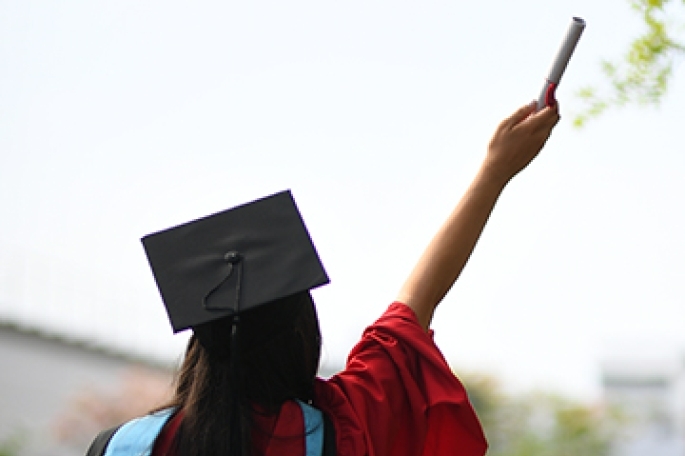 Student in commencement attire holding up scroll