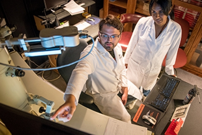A male and female student conducting research while wearing lab coats in the pharmacy research lab at St. John’s University