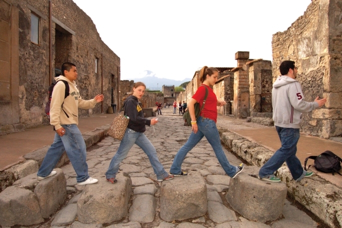 4 people cross large rocks on a path