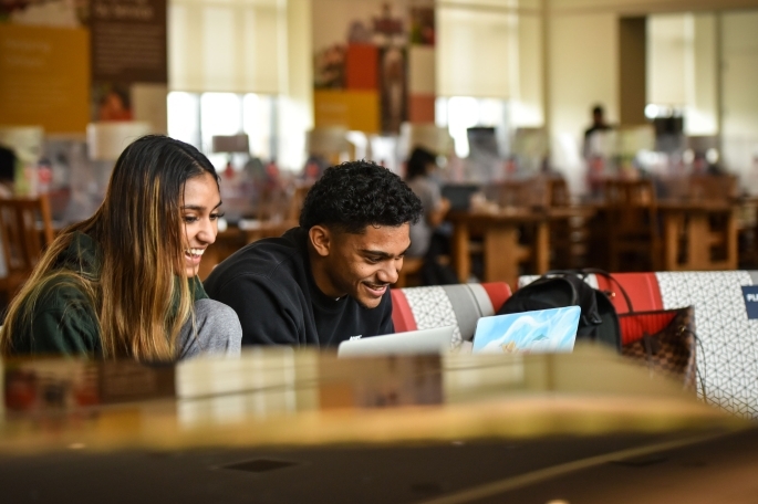 Female and male student sitting at long desk working on laptops