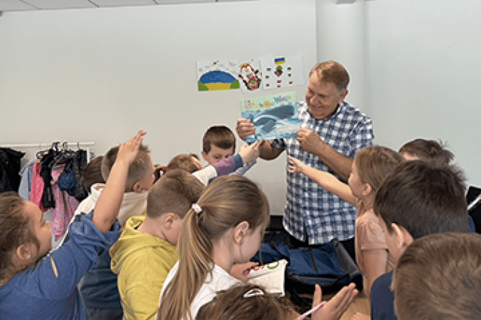 Sampson holding up children's book while surrounded by Ukrainian refugee children