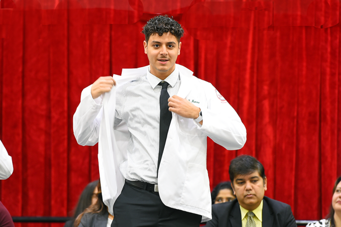 student putting on his white coat at Pharmacy White Coat Ceremony