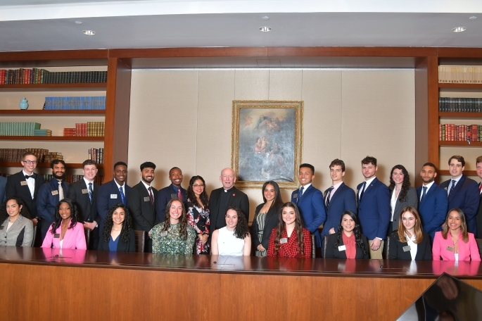 Two rows of alumni sitting behind a long desk posing for a group photo