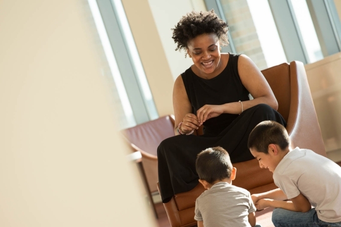 Female student sitting in a chair watching over two male children playing