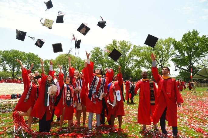 Students in red gowns throwing their black caps in the air after graduating